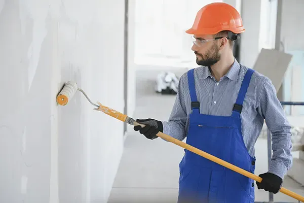 Profissional com capacete e óculos de proteção pintando parede em obra comercial