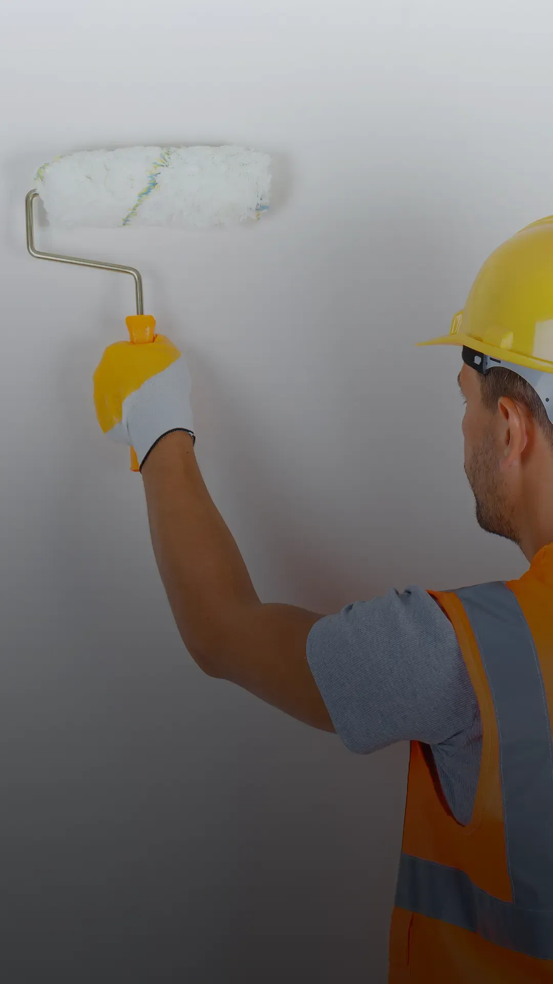 Profissional com capacete e colete de segurança pintando parede em ambiente corporativo