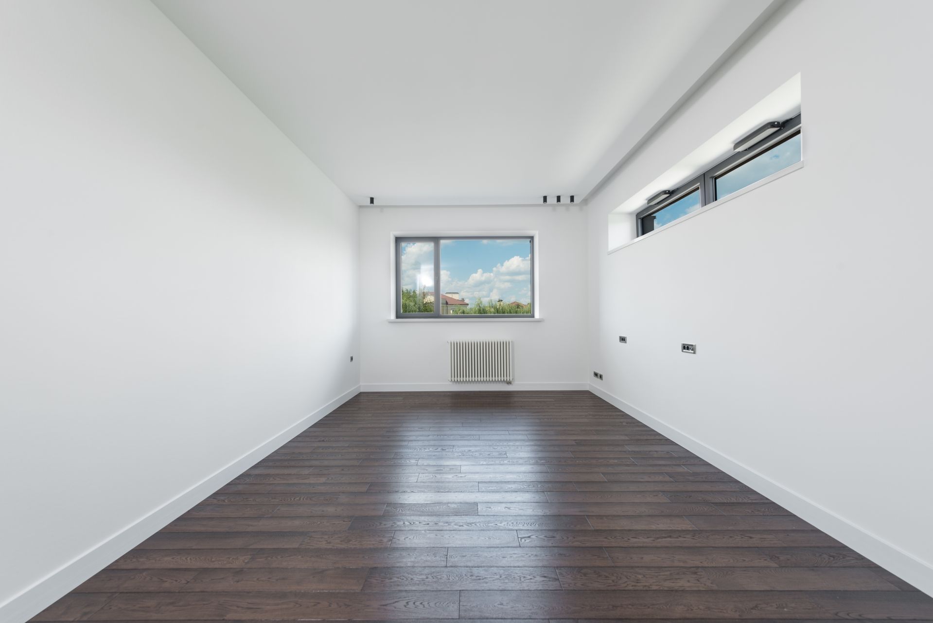 Quarto amplo com paredes brancas pintadas e piso de madeira escura